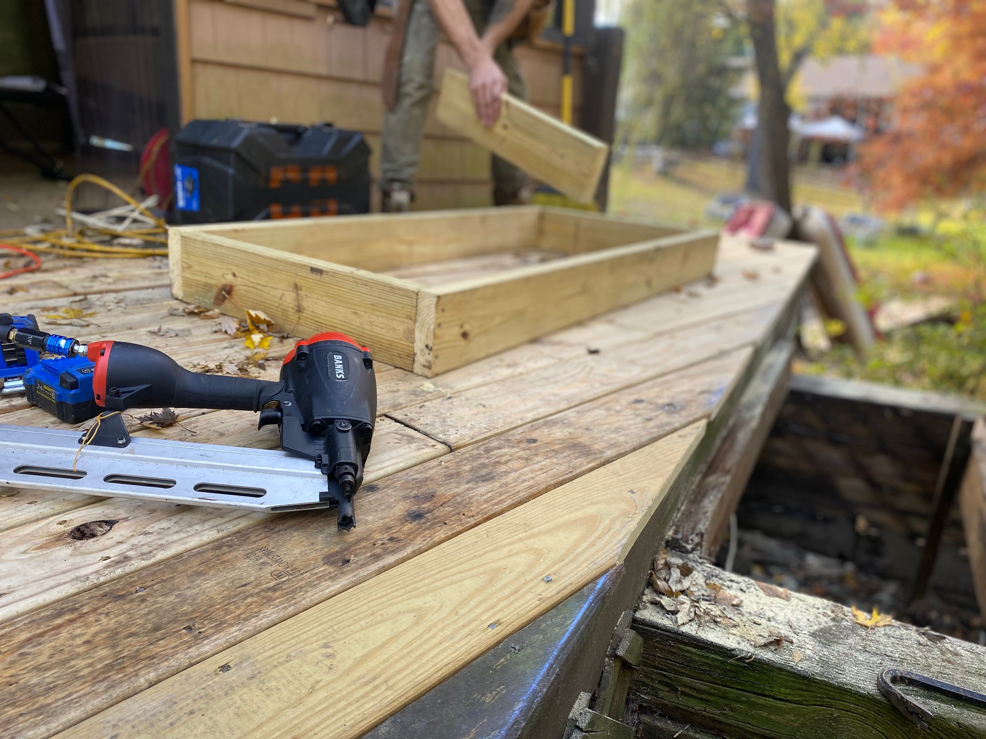 Close-up of deck construction showing a nail gun, decking boards, and the supporting wood frame